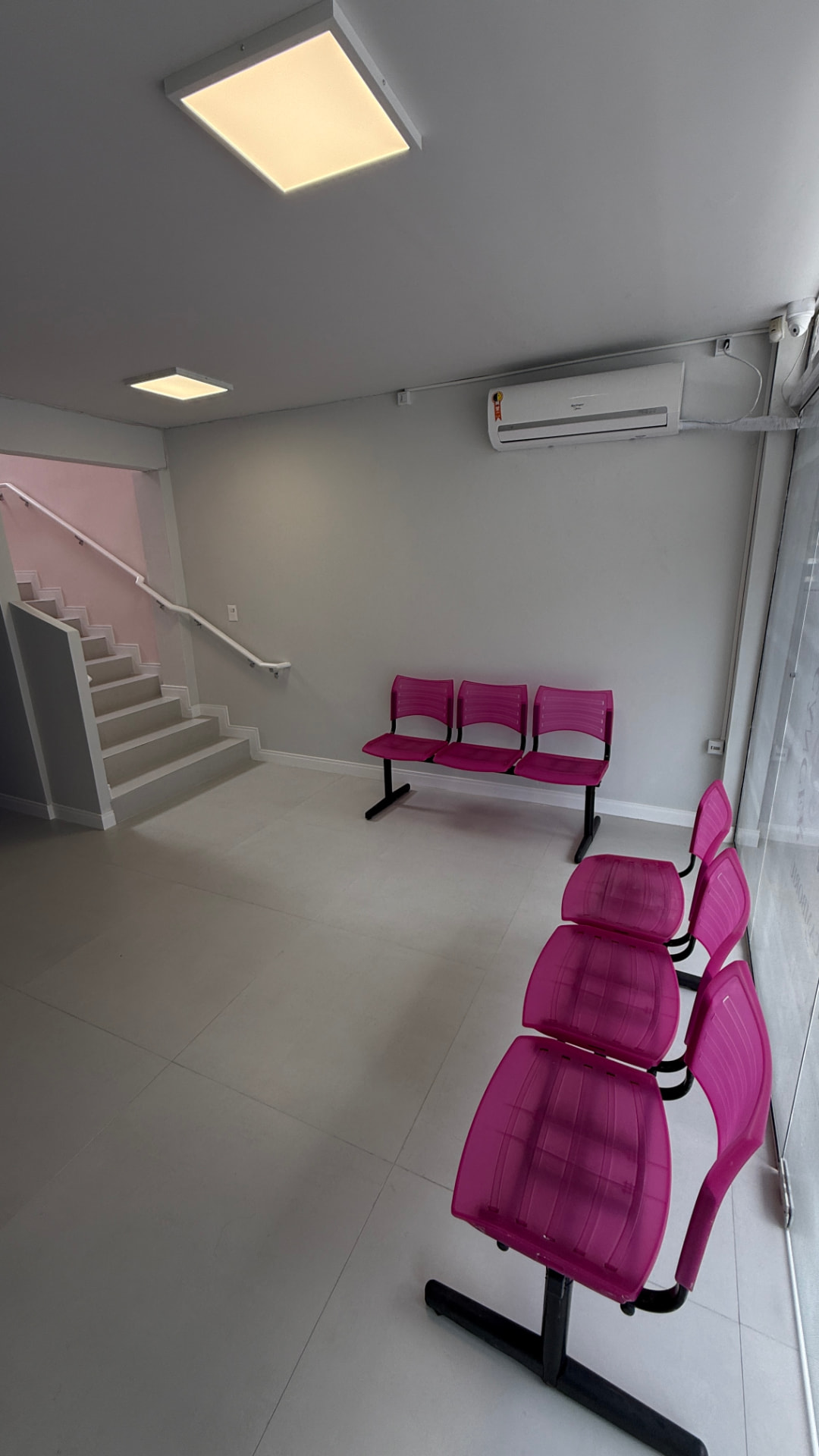 Recepção da instituição, com fileiras de cadeiras cor-de-rosa e escada que leva ao piso superior